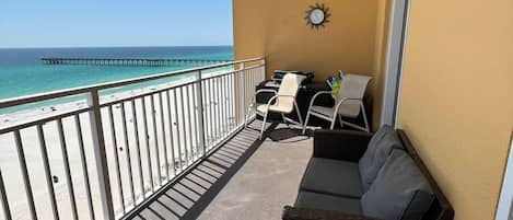 A balcony with a view of the ocean and a pier, furnished with a sofa and chairs.