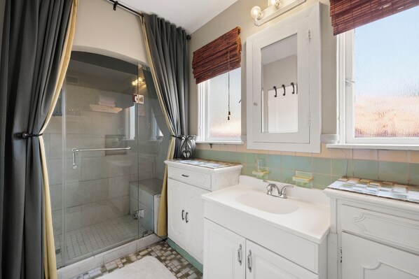 Un baño con cabina de ducha de vidrio, un lavabo blanco y un tocador con armarios.