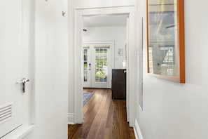 A hallway with wooden flooring leading to a door with glass panels, a dark cabinet, and a framed picture on the wall.