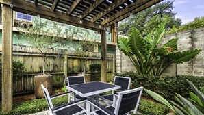 An outdoor patio with a wooden pergola, a table with chairs, and various plants.