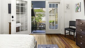 A bedroom with a bed, a dresser, a chair, and a door leading to an outdoor patio with a table and chairs.