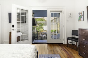 Une chambre à coucher comprenant un lit, une commode, une chaise et une porte donnant sur un patio extérieur avec une table et des chaises.