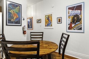 A dining area with a round wooden table and four chairs, surrounded by white walls with framed posters.