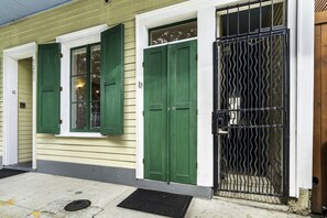 A building with two green doors, a barred gate, and a window with a curtain.