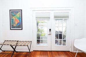 A room with a white door, a framed poster on the wall, a wooden floor, and a white chair. - Pelican Point - Lovely Apartment / Backyard (New Orleans)