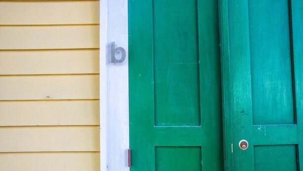 A green door with a white letter 'b' on a yellow wall.
