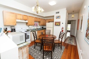 A compact kitchen with wooden cabinets, a dining table with chairs, a refrigerator, and a microwave. - Pelican Point - Lovely Apartment / Backyard (New Orleans)