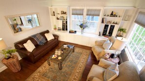 A living room with a brown leather sofa, beige armchairs, a coffee table, and a large window with a view of greenery. - Boyer Place · Boyer Place, Updated Home - Walk to Campus & Town (Walla Walla)