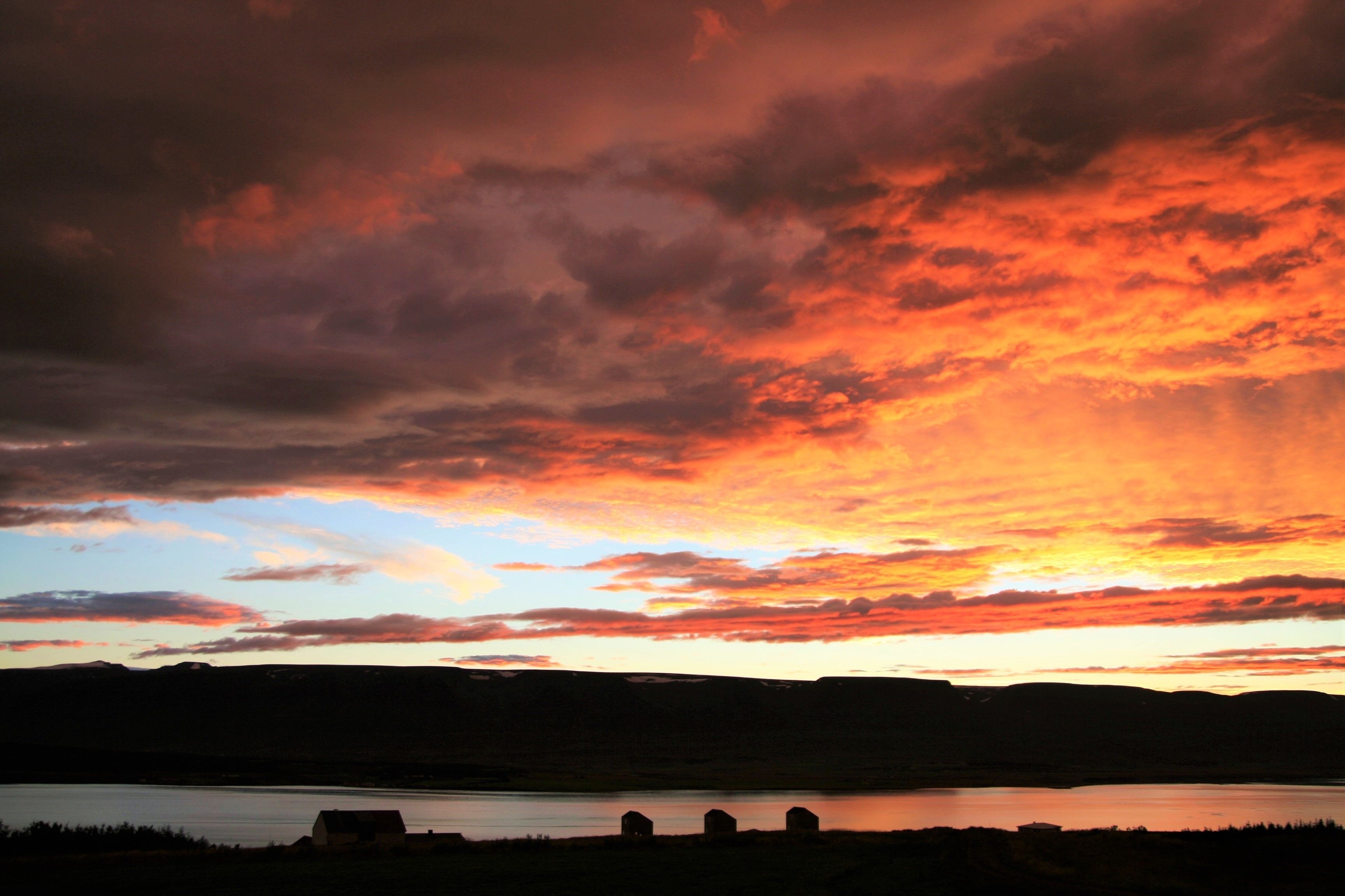 A sunset over a lake with three buildings silhouetted against the sky.