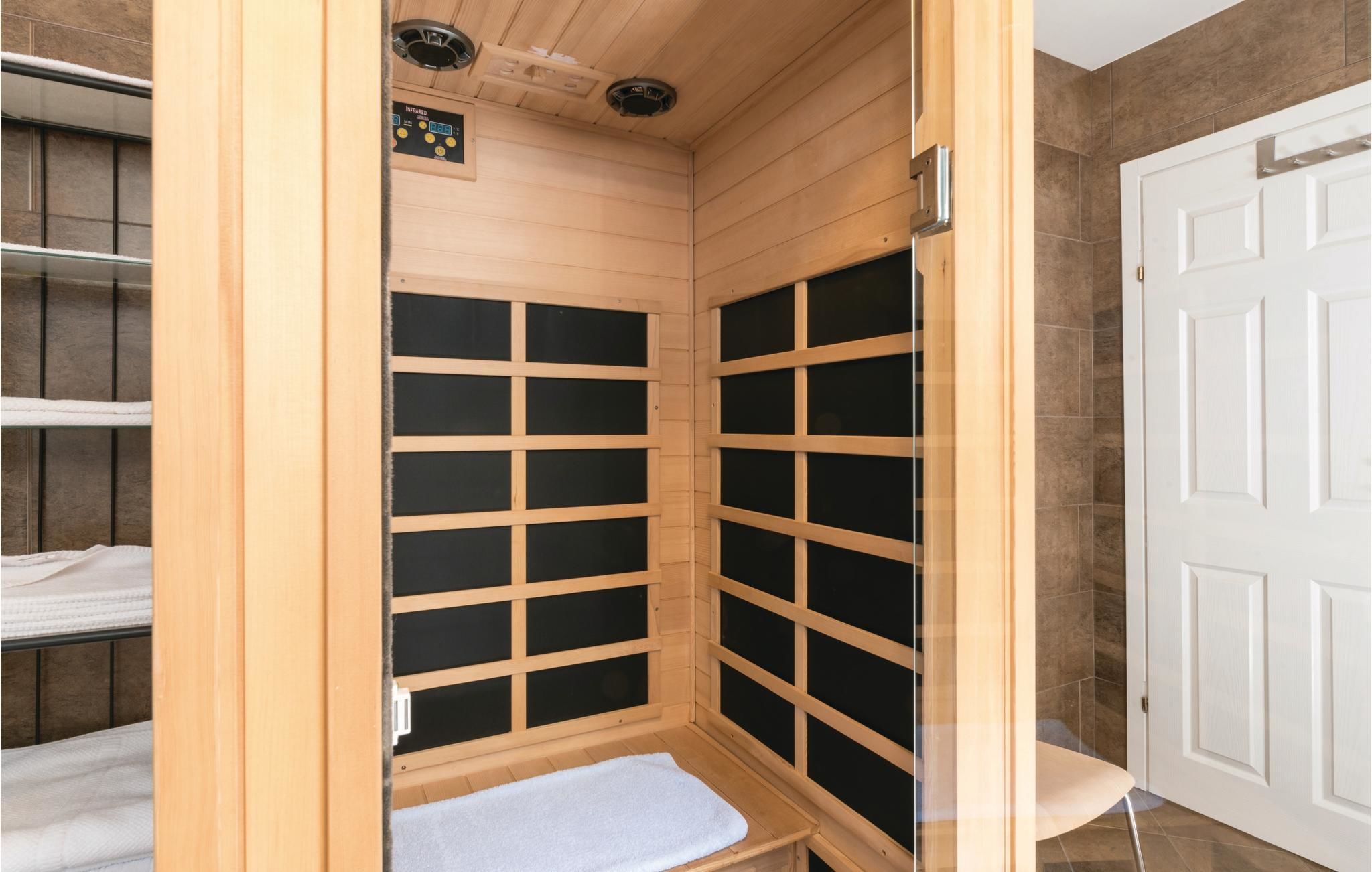 A sauna room with wooden walls, a bench, and a control panel.