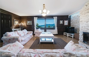 A cozy living room with a fireplace, floral sofas, a coffee table, and a large window offering a scenic view. - Awesome Home in Lepajci w/ Sauna, Wifi and 3 Bedrooms (Krapina)