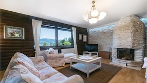 A cozy living room with a stone fireplace, floral sofas, a television, and a large window offering a scenic view. - Awesome Home in Lepajci w/ Sauna, Wifi and 3 Bedrooms (Krapina)