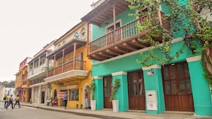 Una strada con edifici colorati, tra cui un edificio verde con un balcone e uno giallo con un cartello.