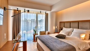 Une chambre d’hôtel moderne avec un grand lit, une table en verre et une vue sur la ville grâce à de grandes fenêtres.