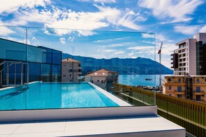 A rooftop pool with a glass barrier, offering a view of a coastal town and mountains. - Hotel Fagus by Aycon (Budva)