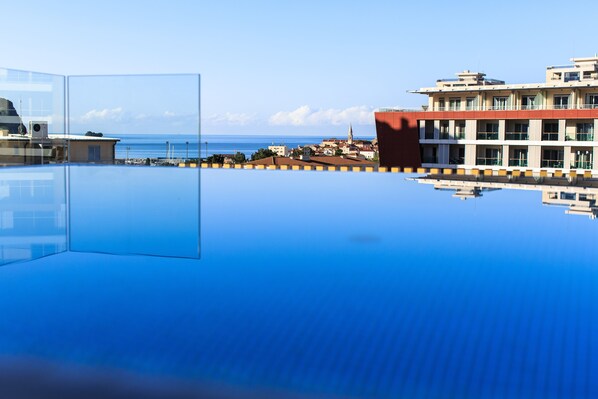 A clear view of a swimming pool with a reflection of a building and the sea. - Hotel Fagus by Aycon (Budva)