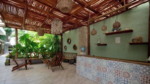 A reception area with a tiled floor, wooden furniture, a green wall with decorative elements, and a bamboo ceiling. - Casa Delia Hotel (Bacalar)