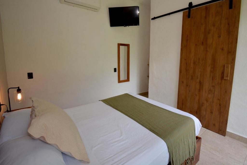A bedroom with a bed, a television mounted on the wall, a wooden door, and a small mirror.