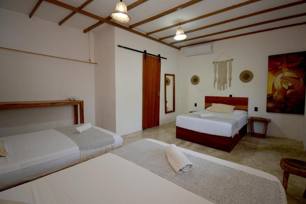 Una habitación con dos camas, un cabecero de madera, una mesita de noche pequeña, un espejo fijado a la pared y un cuadro.