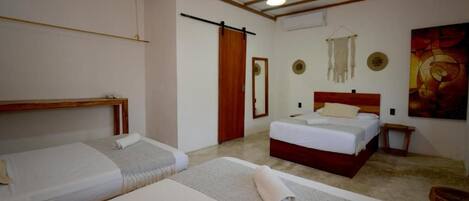 Una habitación con dos camas, un cabecero de madera, una mesita de noche pequeña, un espejo fijado a la pared y un cuadro.