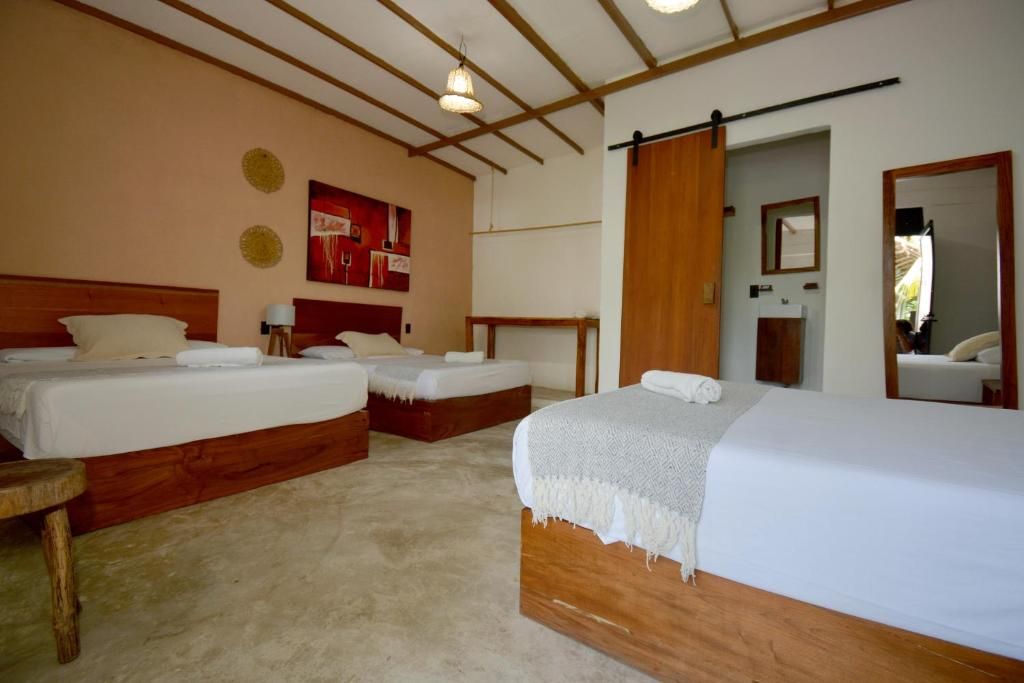 Habitación de hotel con dos camas, cabecero de madera, un espejo grande y una puerta que da a otra habitación.