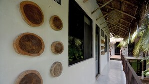 A covered walkway with a thatched roof, wooden wall decorations, and a view of greenery outside. - Casa Delia Hotel (Bacalar)