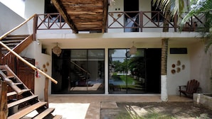 A wooden staircase leading to a balcony with a thatched roof, a glass door entrance, and a small outdoor seating area with a chair. - Casa Delia Hotel (Bacalar)