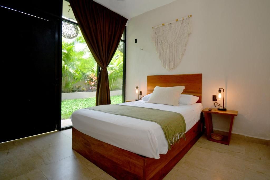 Une chambre avec un grand lit, une tête de lit en bois, une table de chevet avec une lampe, et une vue sur la verdure à l’extérieur.