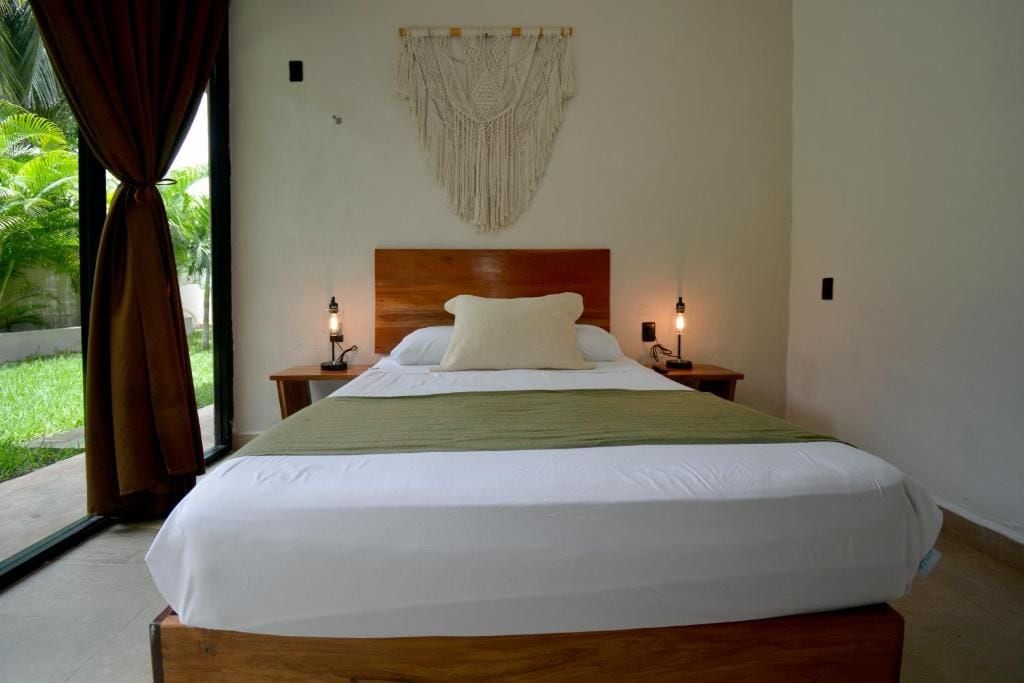 A hotel room with a large bed, two bedside tables, a wooden headboard, and a macrame wall hanging.