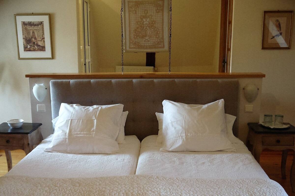A double bed with white linens, a wooden headboard, and two bedside tables with lamps.