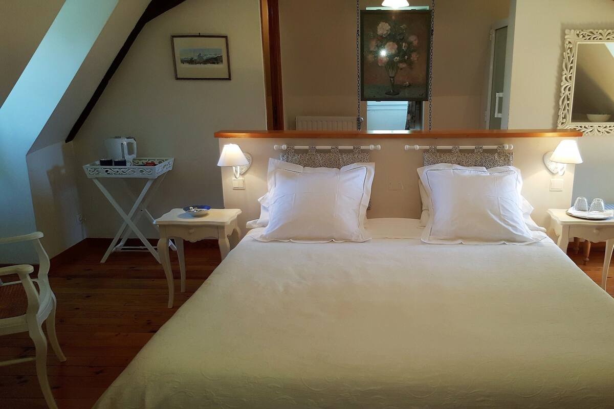 A bedroom with a large bed, two bedside tables with lamps, a small table with a bowl, and a chair.