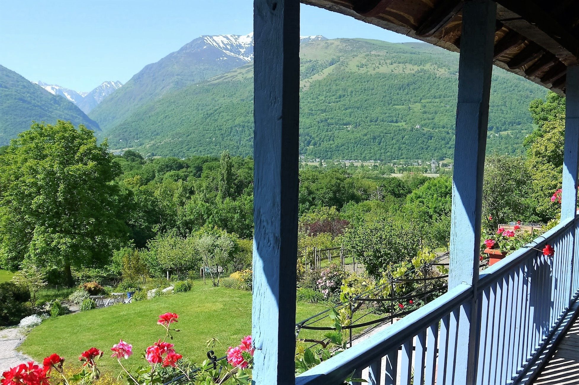 A balcony with a view of a mountainous landscape and a garden with red flowers.