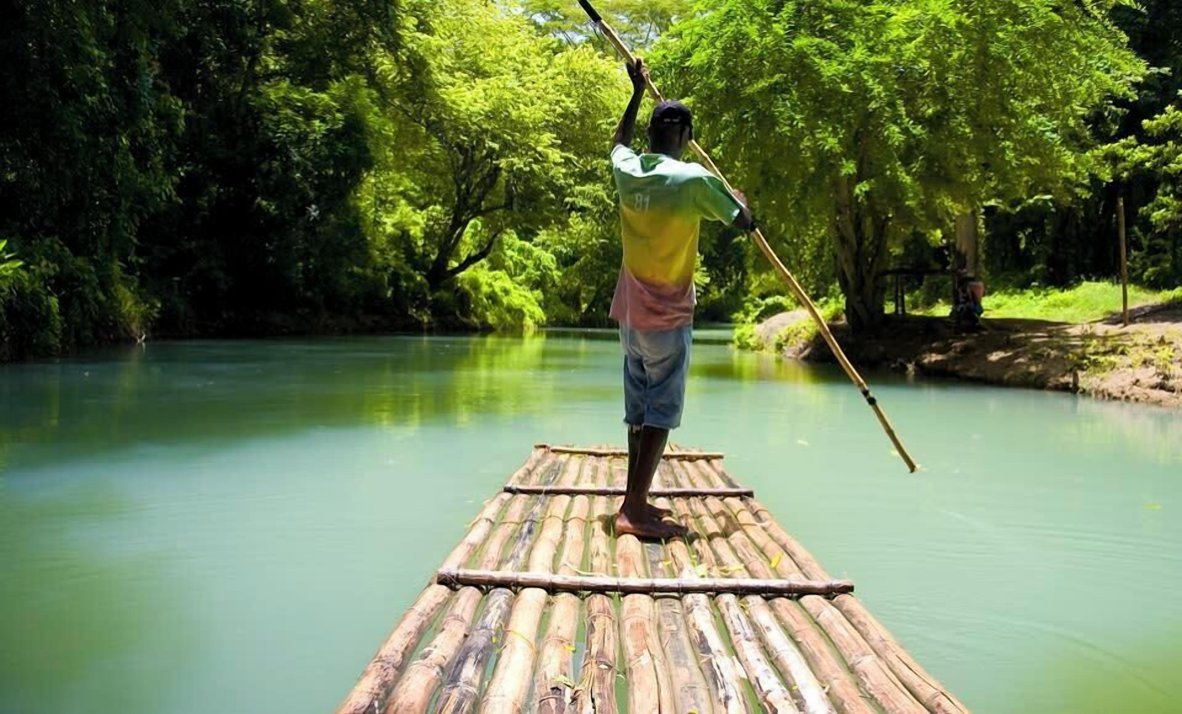A person standing on a bamboo raft in a river surrounded by dense greenery.