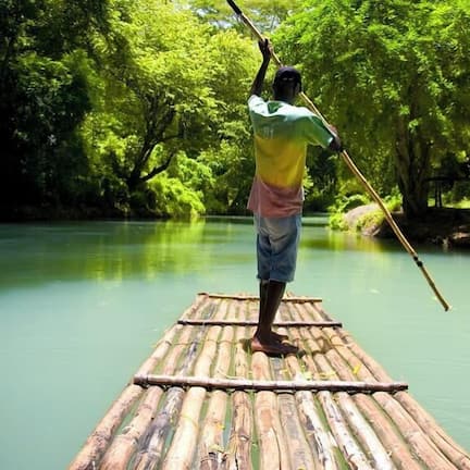 A person standing on a bamboo raft in a river surrounded by dense greenery.