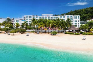 A beachfront hotel with multiple floors, palm trees, and beach umbrellas.