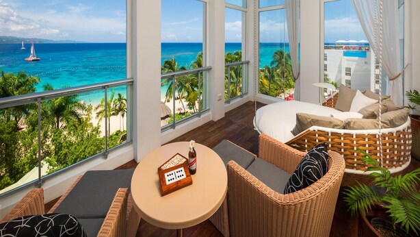 A balcony with a view of the ocean, wicker furniture, and a table with a board game.