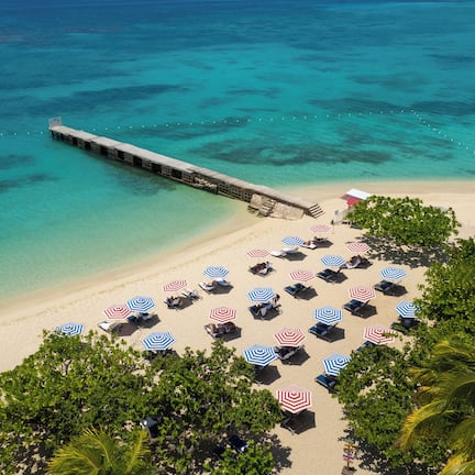 A beach with a pier extending into the water, surrounded by beach umbrellas and lounge chairs.