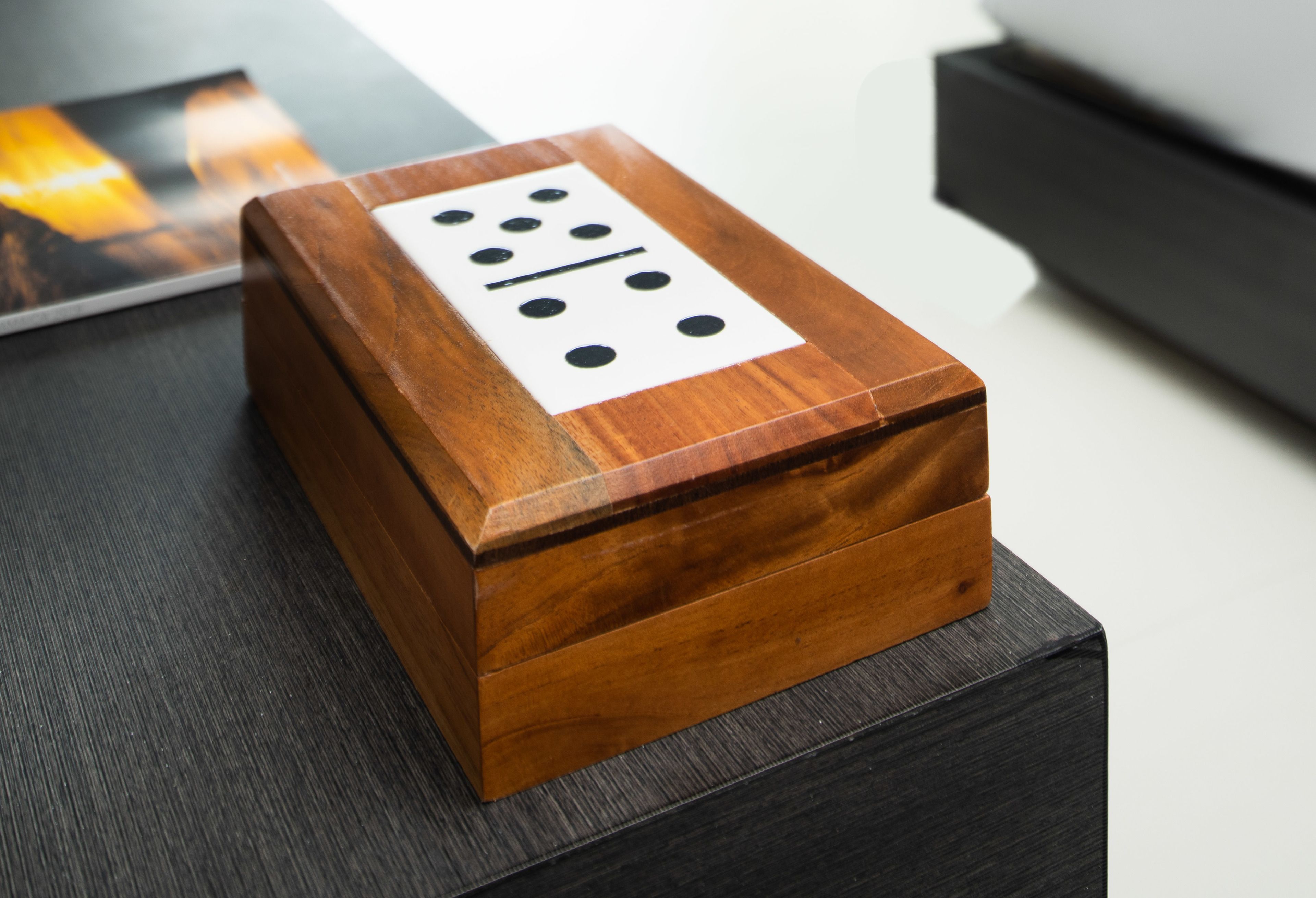 A wooden box with a white label featuring black dots and lines, placed on a dark surface.