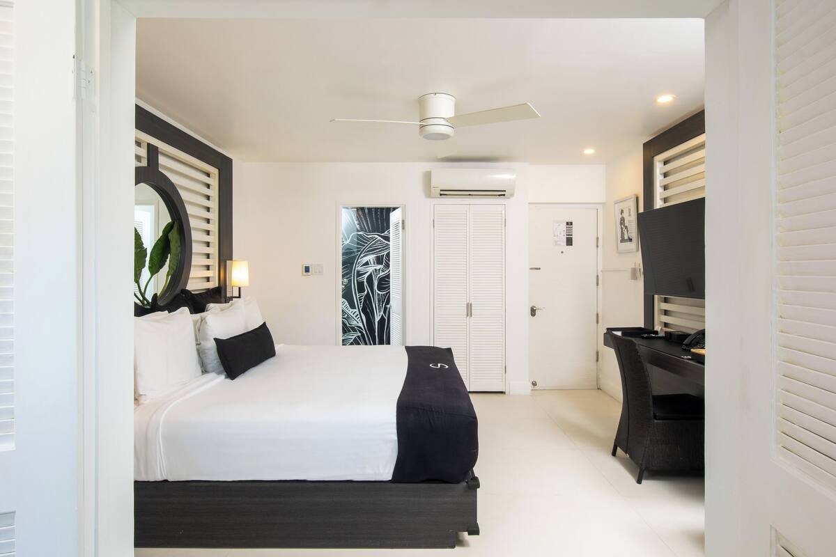 Un dormitorio con cama, escritorio, silla, ventilador de techo y una puerta.