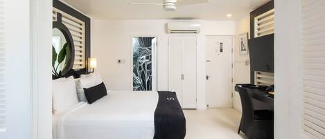 A bedroom with a bed, a desk, a chair, a ceiling fan, and a door.