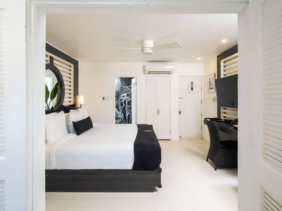 A bedroom with a bed, a desk, a chair, a ceiling fan, and a door.