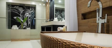 A modern bathroom with a large mirror, a wooden wall, a shower with a chrome faucet, and a wicker chair.