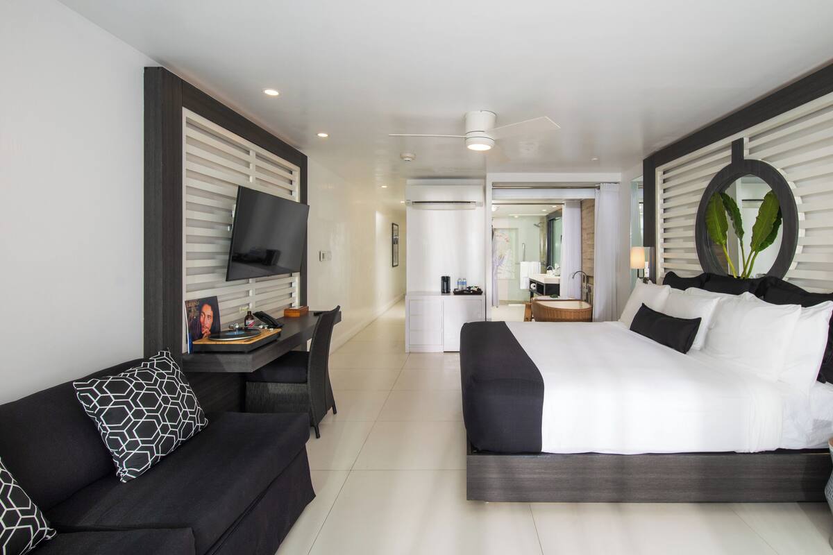 Habitación de hotel moderna con una cama grande, un televisor, un escritorio con una computadora y un baño visible a través de una puerta abierta.