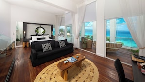 A modern living room with a black sofa, a wooden coffee table, and a large window offering a view of the ocean.
