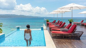 A poolside area with lounge chairs and umbrellas, overlooking a body of water and distant land.