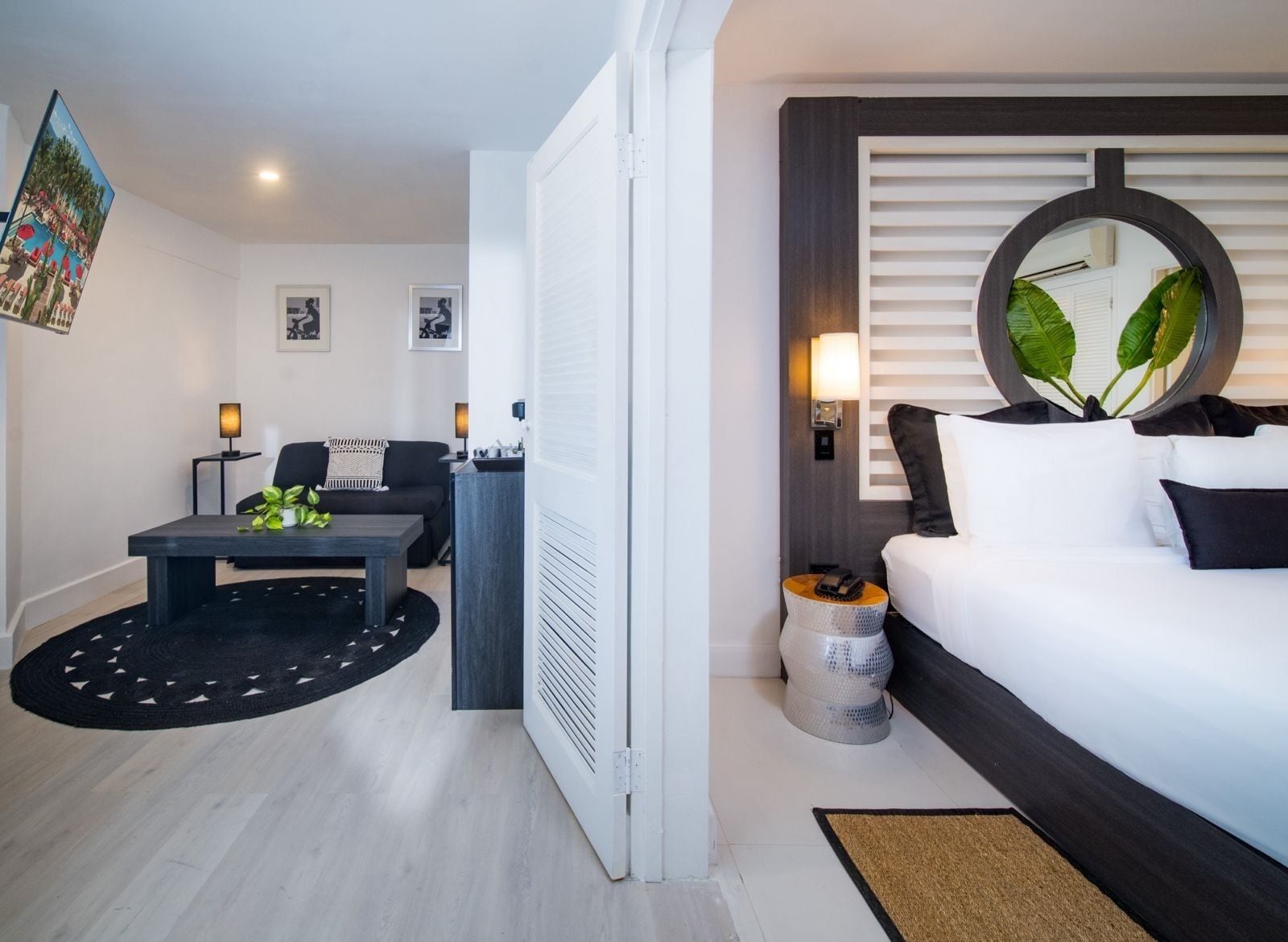 Una habitación de hotel moderna con cama, escritorio, silla, mesita y espejo redondo.