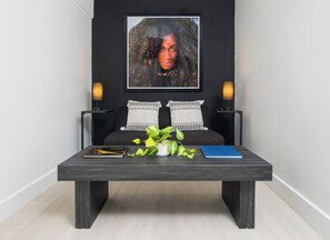 A modern living room with a dark sofa, two side tables with lamps, a coffee table with a plant and books, and a framed artwork above the sofa.