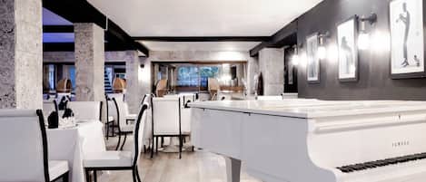 A spacious room with a grand piano, white chairs, and a dining area.