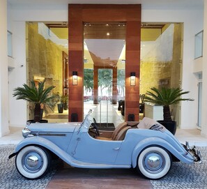 A vintage blue convertible car parked in front of a hotel entrance with a modern interior and large windows.