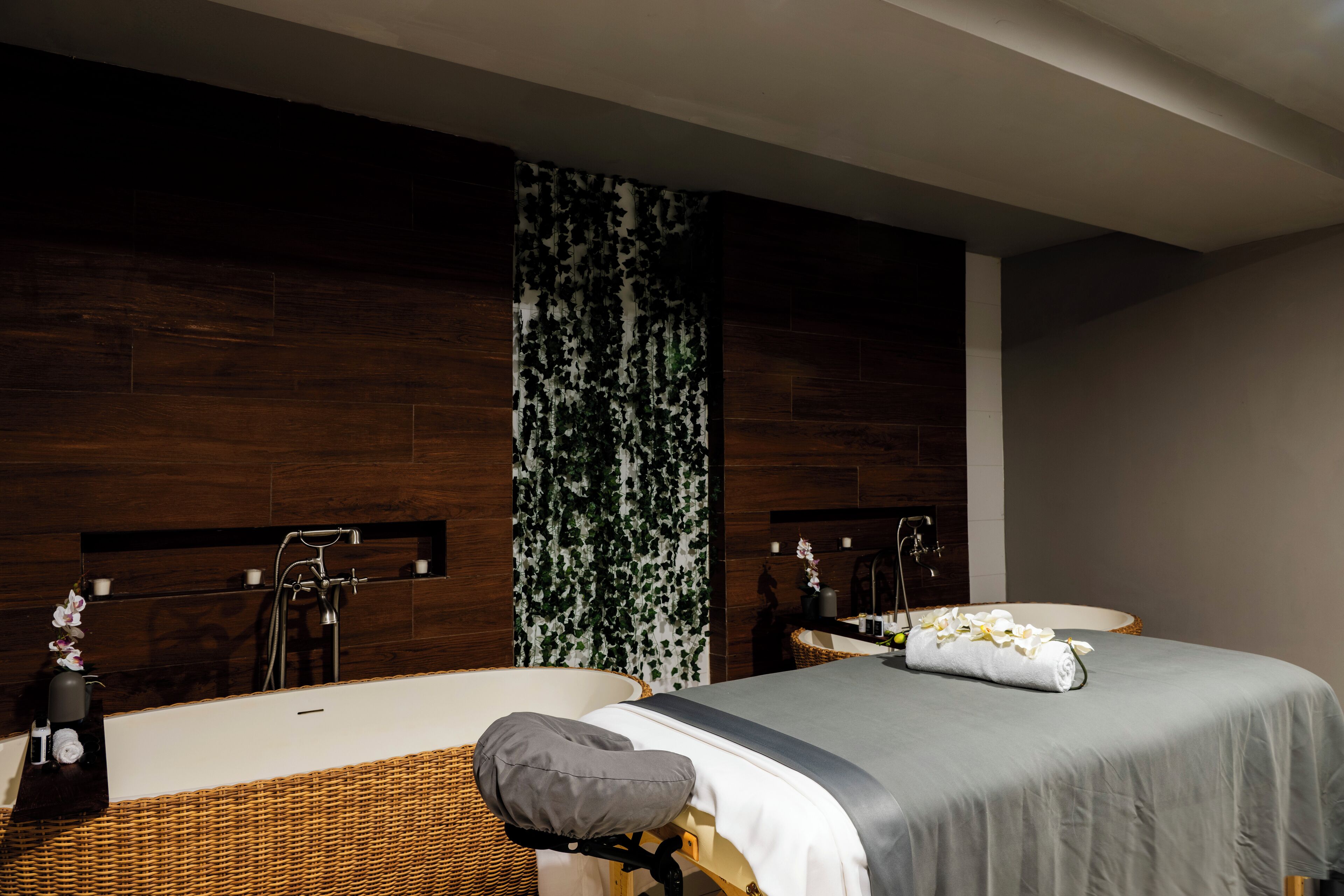 A modern bathroom with a bathtub, a large mirror, and a bed with a towel and flowers.